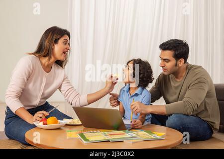 Mère nourrissant de la pomme à son fils tout en faisant des devoirs avec le père Banque D'Images