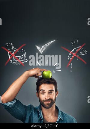 IVE a fait le bon choix. Studio portrait d'un beau jeune homme debout avec une pomme sur sa tête contre une illustration de ses choix contre Banque D'Images