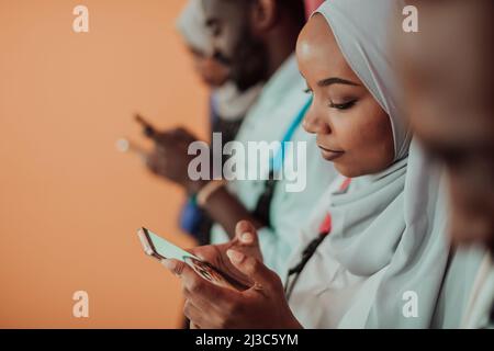Un groupe d'étudiants musulmans africains utilisent un smartphone tout en se tenant devant un fond jaune Banque D'Images