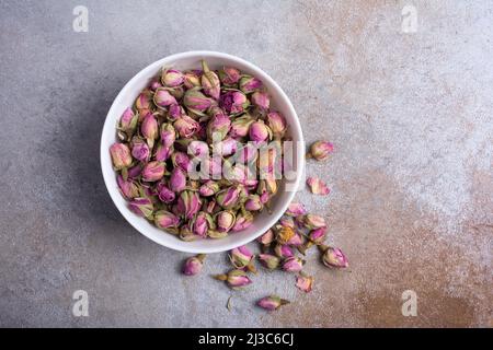 Vue de dessus d'un bol blanc avec boutons de rose séchés pour le thé parfumé sur fond de béton gris Banque D'Images