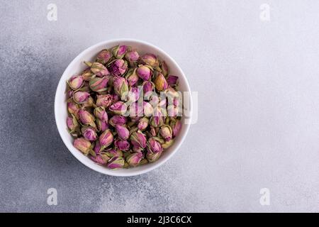 Vue de dessus d'un bol blanc avec boutons de rose séchés pour le thé parfumé sur fond de béton gris Banque D'Images