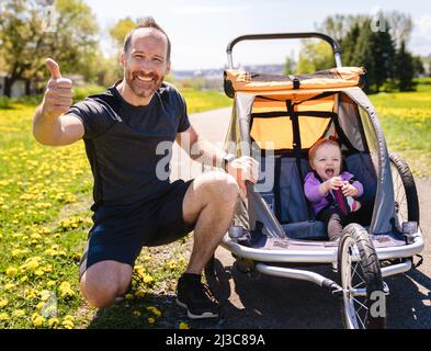 homme avec bébé dans une poussette de jogging en dehors de la saison d'été Banque D'Images