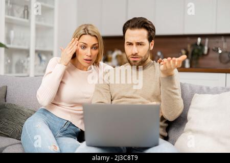 Un jeune couple caucasien a des problèmes financiers. Une femme frustrée et un mari contrarié à regarder des factures sur l'ordinateur portable. Jeunes conjoints incapables de payer l'hypothèque Banque D'Images