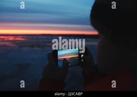 Homme mains avec un téléphone portable prenant une photo du ciel de coucher de soleil en mer. Couleur de dégradé. Texture du ciel. Beau coucher de soleil abstrait nature comme arrière-plan Banque D'Images