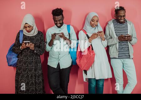 Un groupe d'étudiants musulmans africains utilisent un smartphone tout en se tenant devant un fond rose Banque D'Images