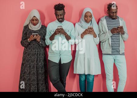 Un groupe d'étudiants musulmans africains utilisent un smartphone tout en se tenant devant un fond rose Banque D'Images