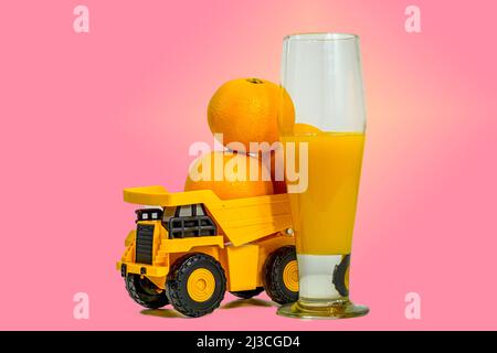 un verre de jus d'orange à côté d'un jouet de camion chargé d'orange sur fond rose Banque D'Images