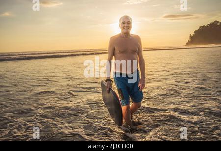 Homme avec planche de Boogie sur la plage au coucher du soleil Banque D'Images