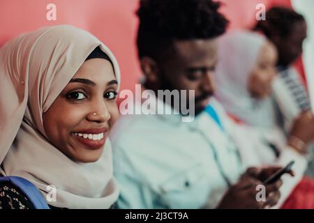 Un groupe d'étudiants musulmans africains utilisent un smartphone tout en se tenant devant un fond rose Banque D'Images