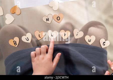 Vue de dessus de crop anonyme enfant pointant vers l'inscription No Bulliting sur les petits coeurs tout en étant assis à la table en verre dans la chambre Banque D'Images