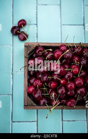 Vue de dessus de la caisse en bois avec un bouquet de cerises fraîches placées sur une table carrelée le jour de l'été Banque D'Images