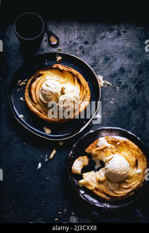 Une tarte aux pommes avec des boules de crème glacée servies sur des assiettes sur une table en marbre foncé Banque D'Images