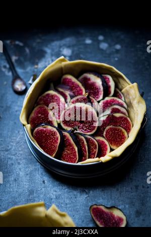 Du dessus du moule à pâtisserie avec de la pâte crue et des tranches de figues placées sur une table gris foncé Banque D'Images