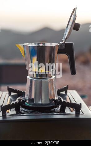 Pot en métal avec couvercle ouvert placé sur le poêle à gaz portable pour préparer du café frais aromatique dans le camping Banque D'Images