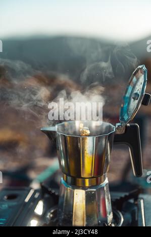 Pot en métal avec couvercle ouvert placé sur le poêle à gaz portable pour préparer du café frais aromatique dans le camping Banque D'Images