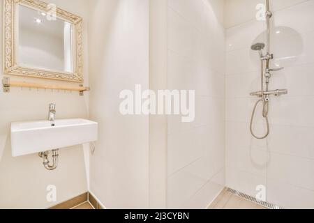 Lavabo en céramique blanc placé au mur avec miroir carré près de la douche avec tuyau en acier inoxydable dans la salle de bains élégante et lumineuse à la maison Banque D'Images