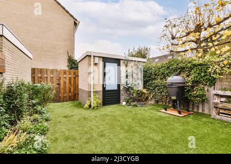 Barbecue moderne placé sur une pelouse verte dans la cour du cottage avec une végétation luxuriante en été Banque D'Images