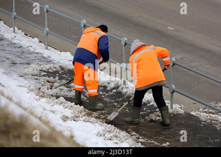 Déneigement et fonte de glace au printemps, deux concierges avec des pelles nettoyant le trottoir sur le fond de la route Banque D'Images