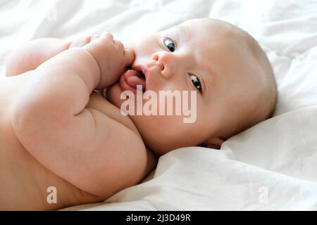 Gros plan Portrait d'un bébé magnifique sur blanc. Tête et visage. Nouveau-né bébé couché sur le côté et regarde dans la caméra. Bébé mignon et adorable Banque D'Images