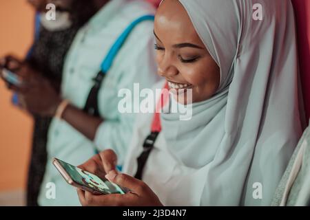 Un groupe d'étudiants musulmans africains utilisent un smartphone tout en se tenant devant un fond jaune Banque D'Images