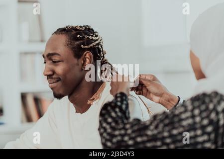 Un jeune couple musulman a un moment romantique à la maison tandis que la femme fait la coiffure pour son mari femme portant le hijab islamique traditionnel du Soudan Banque D'Images