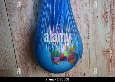 Le globe terrestre de la planète Terre est suspendu dans un sac de déchets en plastique bleu sur un fond de planches en bois Banque D'Images