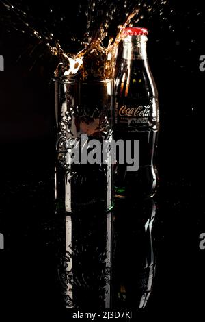 HELSINGBORG, SUÈDE - 06 AVRIL 2022 : une photo en studio d'un cube de glace tombant dans un verre plein de coca cola entraînant une éclaboussure de cola. Banque D'Images