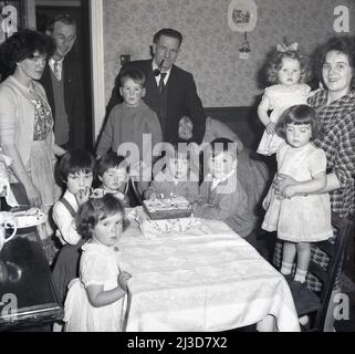 1961, historique, à la maison avec des parents, un ami et grand-père avec pipe, une petite fille, avec d'autres petits enfants, ont leur photo prise avec le gâteau d'anniversaire, un gâteau d'éponge, Stockport, Manchester, Angleterre, ROYAUME-UNI. Banque D'Images