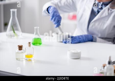 flacons et flacons près d'un assistant de laboratoire flou dans des gants en latex travaillant en laboratoire Banque D'Images
