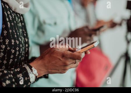 Un groupe d'étudiants musulmans africains utilisent un smartphone tout en se tenant devant un fond rose Banque D'Images