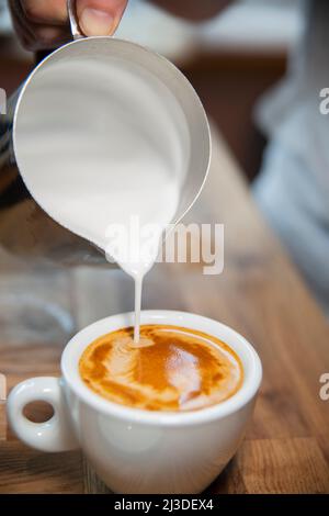Faire un café dans un café - verser le lait à un blanc plat Banque D'Images