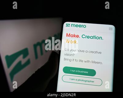 Personne tenant le logo de la société de photographie française Meero sur la page Web du smartphone à l'écran devant le logo. Concentrez-vous sur le centre de l'écran du téléphone. Banque D'Images