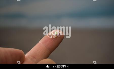 Gros plan de microplastiques sur les doigts humains. Concept de pollution de l'eau et de réchauffement de la planète. L'idée du changement climatique. Banque D'Images