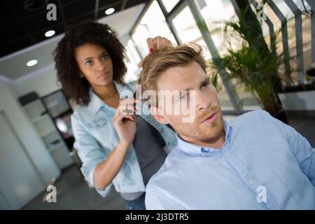 coiffeur souriant coupant les cheveux d'un client masculin au salon Banque D'Images