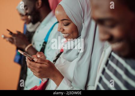 Un groupe d'étudiants musulmans africains utilisent un smartphone tout en se tenant devant un fond jaune Banque D'Images