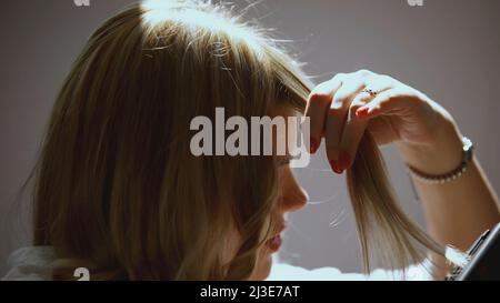 La fille serpente sur un fer à friser. ART. La fille a des cheveux blonds qu'elle boucle. Lisseur cheveux courbés Banque D'Images