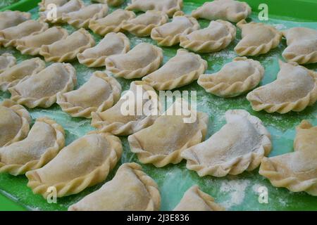 Boulettes non cuites sur un plateau de cuisine vert avec de la farine préparée et prête à cuire. Les boulettes, ou Varényks avec divers remplissages sont traditionnels UKR Banque D'Images