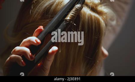 La fille serpente sur un fer à friser. ART. La fille a des cheveux blonds qu'elle boucle. Lisseur cheveux courbés Banque D'Images