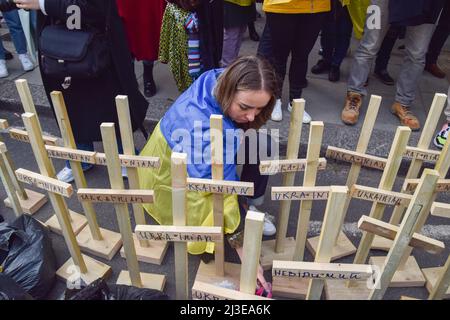 Londres, Angleterre, Royaume-Uni. 7th avril 2022. Un manifestant enveloppé dans un drapeau de l'Ukraine place des chaussures pour enfants à côté de croix en bois portant les inscriptions 'Ukrainian'. Des centaines de personnes se sont rassemblées devant l'ambassade de Russie et ont jeté des casseroles, des vêtements, des jouets, des appareils et d'autres articles ménagers, en réponse au pillage par les soldats russes en Ukraine. (Image de crédit : © Vuk Valcic/ZUMA Press Wire) Banque D'Images