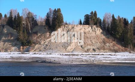 Paysage naturel avec une rivière au début de l'hiver et une côte vallonnée couverte d'arbres. Attache. Falaise en pierre avec forêt et rivière froide. Banque D'Images