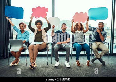 Ils sont un groupe vivant. Portrait d'un jeune groupe joyeux de collègues de travail assis les uns à côté des autres tout en tenant des panneaux à l'intérieur du bureau Banque D'Images