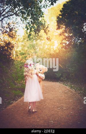 Je me demande où cela mène. Photo d'une petite fille méconnaissable marchant avec son ours en peluche au milieu d'une route de terre. Banque D'Images