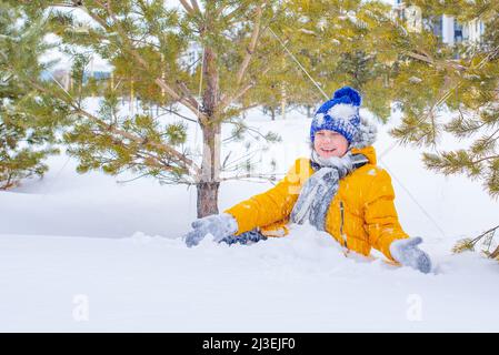 dans une veste jaune et un chapeau bleu garçon jouant dans la neige Banque D'Images