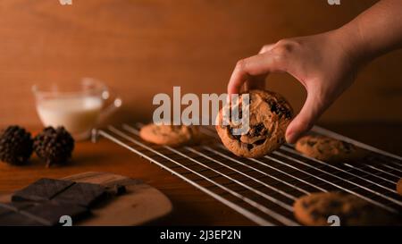 Les femmes rasent un morceau de biscuits aux pépites de chocolat fraîchement cuits sur le panier de refroidissement. Banque D'Images