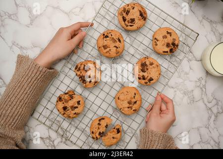 Vue de dessus, femelle tenant un plateau de biscuits aux pépites de chocolat fraîchement cuits sur fond de table en marbre Banque D'Images