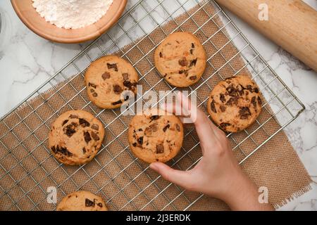 Au-dessus de la tête, les mains des femmes ramassant des biscuits aux pépites de chocolat fraîchement cuits. Délicieux petits gâteaux faits maison. Banque D'Images