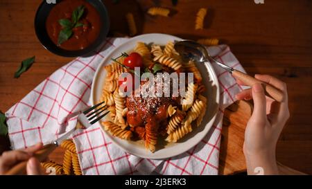 En gros plan, la femme mange de savoureuses pâtes italiennes de fusilli à la tomate avec fourchette et cuillère dans une table à manger vintage. Banque D'Images