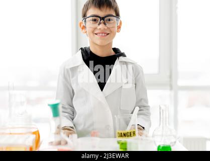 Garçon d'école portant des lunettes de protection faisant une expérience de chimie en classe de sciences élémentaires. Pupille intelligente regardant l'appareil photo et souriant en laboratoire pendant Banque D'Images
