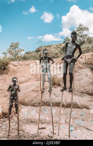 Région des nations du Sud, Éthiopie - 10 mai 2019: Inconnu Joyeux Banna garçon avec la peinture traditionnelle du corps marchant sur des pilotis dans la région des nations du Sud, Banque D'Images