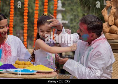 Petite-fille appliquant de la couleur sur le visage du grand-père et mère assise à côté à l'occasion de Holi Banque D'Images